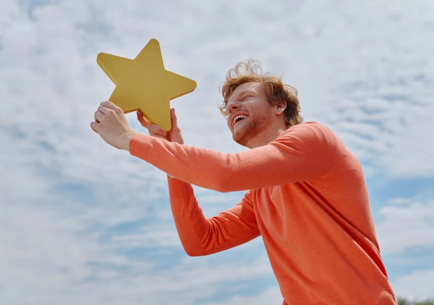 Smiling man in an orange sweater holding a large yellow star above his head against a cloudy sky - illustration for an article about lead scoring