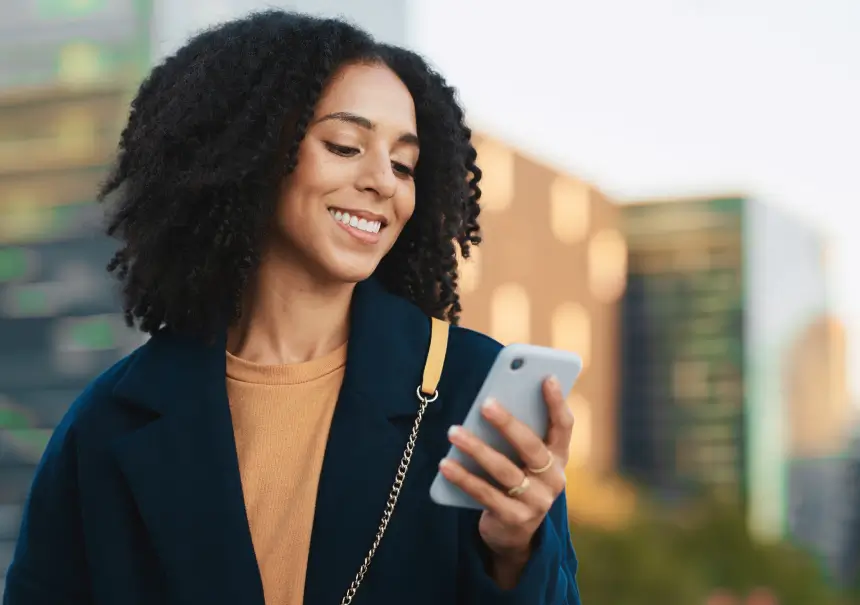 A woman smiling while checking mobile notifications on her smartphone, representing an effective mobile marketing automation strategy for e-commerce.