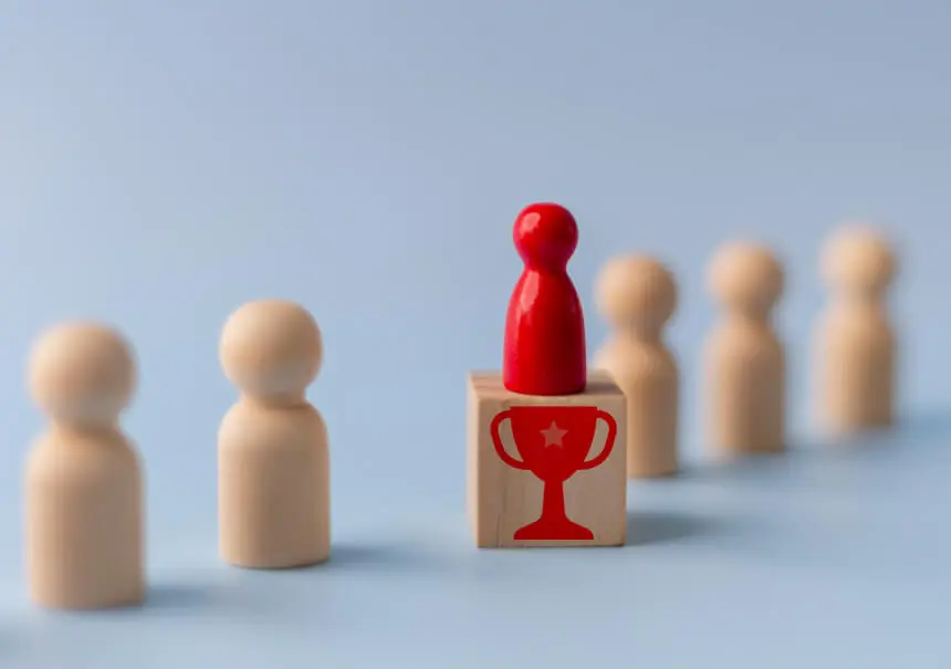 Lead scoring in marketing automation – a red token representing a qualified lead stands on a wooden block with a trophy design, standing out from the other tokens.