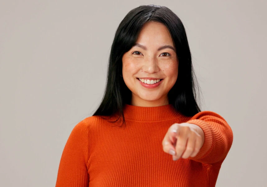 1-to-1 personalization in marketing automation: a smiling woman in an orange turtleneck points her finger toward the viewer, symbolizing direct and individualized customer communication.