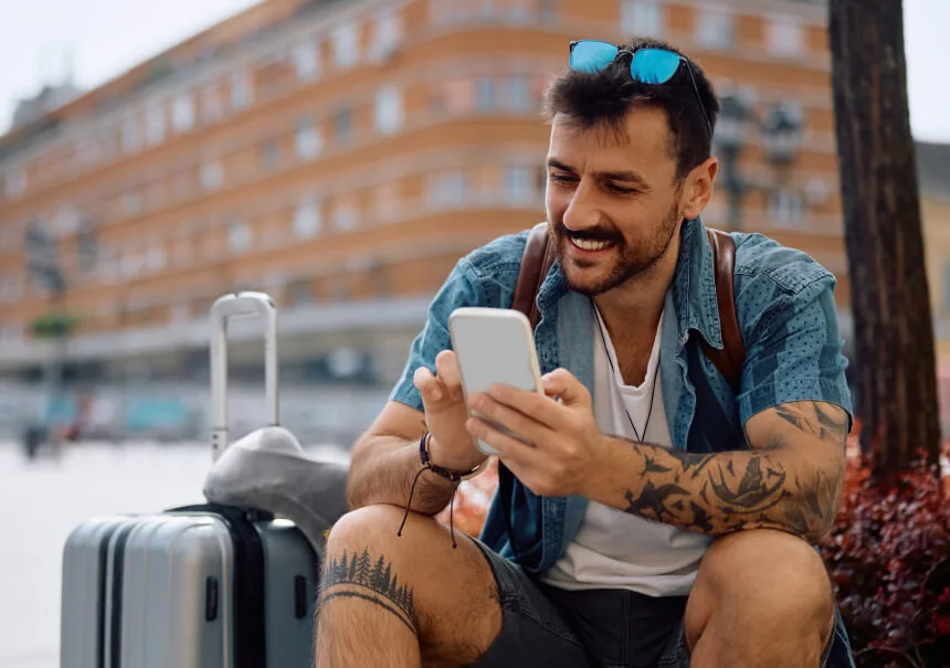Tattooed traveler with a suitcase checking an automated booking confirmation on his smartphone. Effective SMS marketing in the travel industry in Poland.
