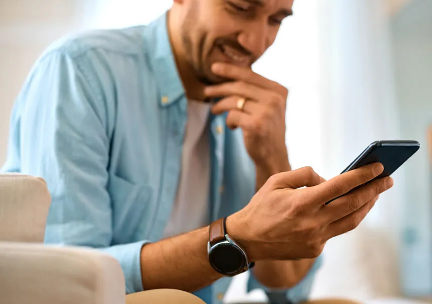 A smiling man curiously reading a personalized push notification on his smartphone screen. A user in a blue shirt with a smartwatch reacting to an engaging web push alert from an online store.