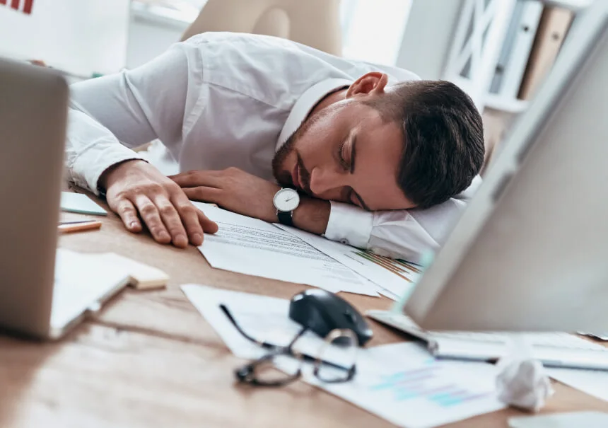 An exhausted marketer sleeping at a desk covered in paperwork. AI and marketing automation take over repetitive manual tasks in the company.