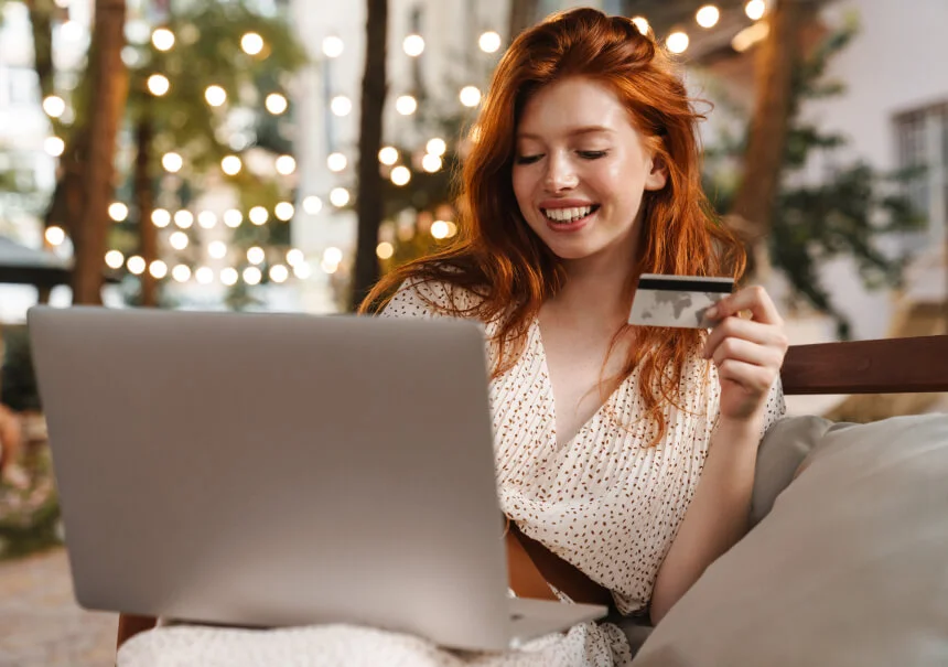 A happy customer holding a credit card while placing an online order on her laptop using a pop-up discount code.
