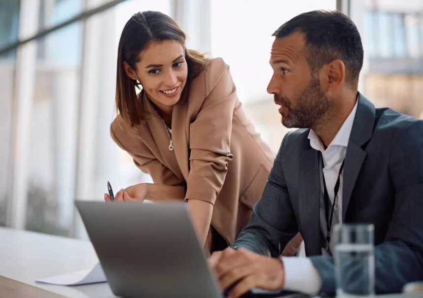 Two financial professionals discussing at a laptop while analyzing personalized email marketing campaigns.