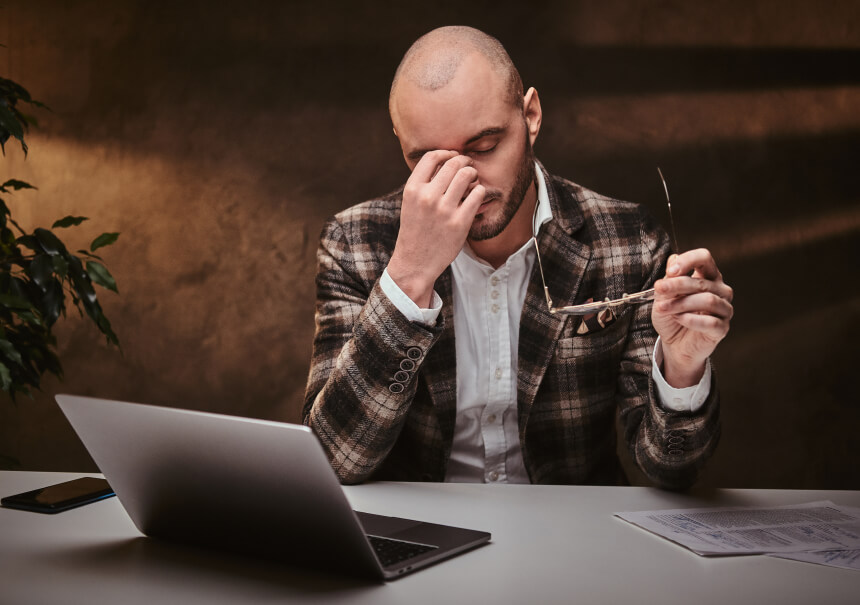 An exhausted businessman rubbing his eyes at a laptop while struggling with manual database management before the peak sales season.